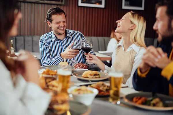 Multiethnic friends sitting at restaurant, drinking alcohol, chatting and having burgers for dinner.