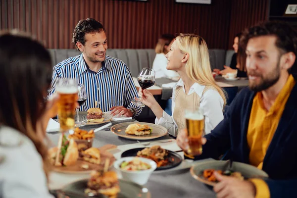 Amis multiethniques assis au restaurant, buvant de l'alcool, bavardant et ayant des hamburgers pour le dîner . — Photo