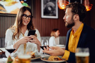 Çok ırklı arkadaşlar restoranda oturan, alkol içme, sohbet ve akşam yemeği için hamburger yeme.