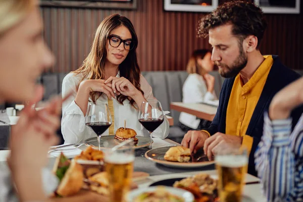 Amigos multiétnicos sentados en el restaurante, bebiendo alcohol, charlando y comiendo hamburguesas para cenar . — Foto de Stock
