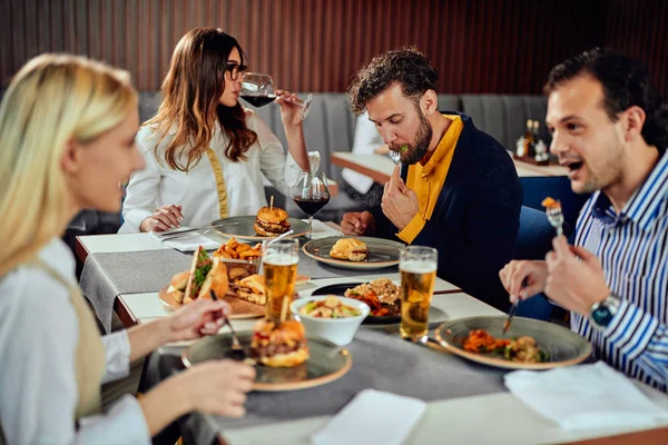Amis multiethniques assis au restaurant, buvant de l'alcool, bavardant et ayant des hamburgers pour le dîner . — Photo