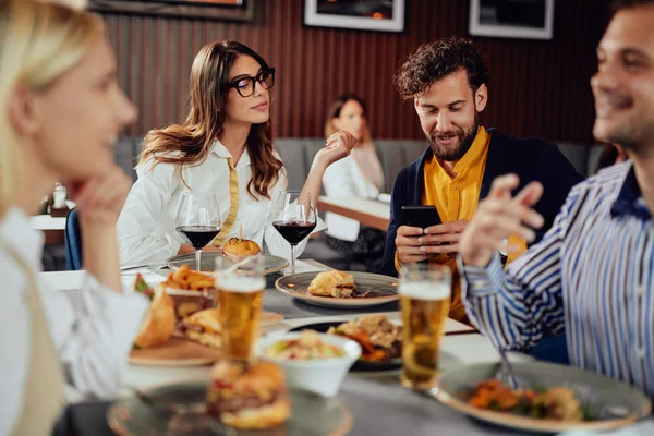 レストランに座っている多民族の友人、アルコールを飲み、おしゃべりをして、夕食にハンバーガーを食べる. — ストック写真