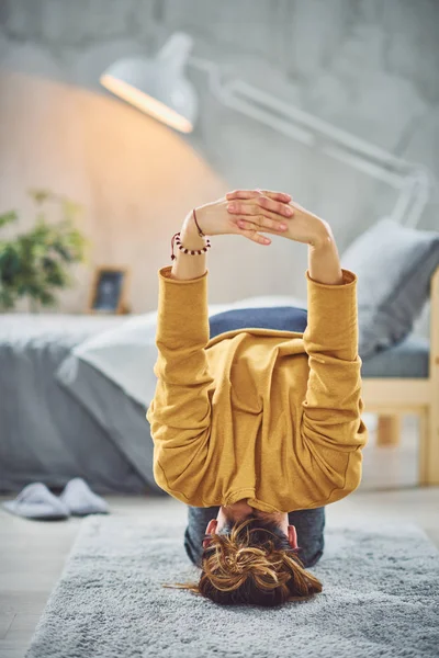 Hermosa morena caucásica haciendo Headstand yoga pose en dormitorio en alfombra . — Foto de Stock
