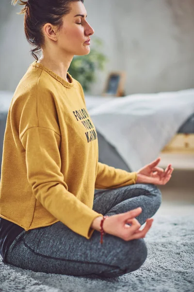 Красива кавказька брюнетка сидить на килимі в спальні в позі Йога для йоги. — стокове фото