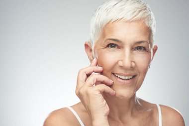 Gri arka plan önünde poz kısa gri saçlı güzel gülümseyen yaşlı kadın. Güzellik fotoğrafçılığı.