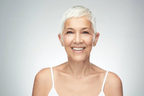 Hermosa mujer mayor sonriente con el pelo gris corto posando delante de fondo gris. Belleza fotografía . —  Fotos de Stock