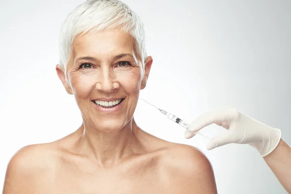 Beautiful smiling Caucasian senior woman standing in front of pink background and taking a shot of anti age product. Beauty photography. — Stock Photo, Image