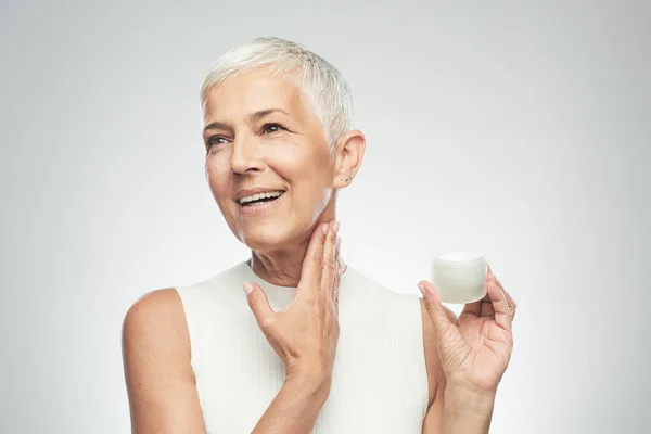 Prachtige glimlachend blanke Senior vrouw uitproberen van nieuwe anti-age crème en kijken naar de camera. Beauty fotografie. — Stockfoto