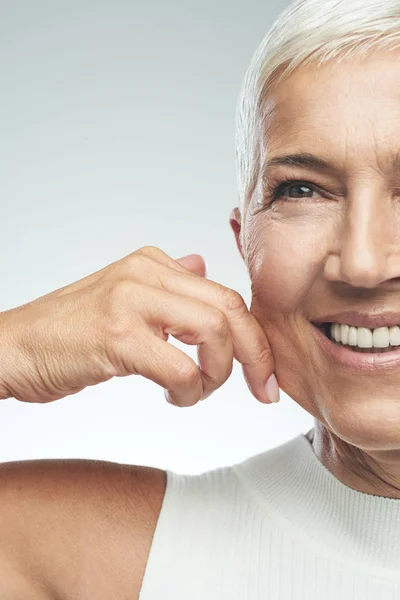 Gorgeous leende kaukasiska Senior Kvinna med kort grått hår klämmande hennes kind. Skönhet fotografi. — Stockfoto