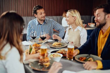 Çok ırklı arkadaşlar restoranda oturan, alkol içme, sohbet ve akşam yemeği için hamburger yeme.