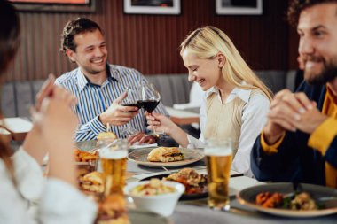 Çok ırklı arkadaşlar restoranda oturan, alkol içme, sohbet ve akşam yemeği için hamburger yeme.
