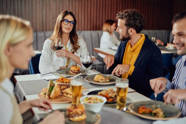 Amis multiethniques assis au restaurant, buvant de l'alcool, bavardant et ayant des hamburgers pour le dîner . — Photo