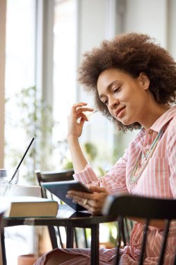 Çekici karışık yarış kadın çizgili pembe elbise kafede oturan ve tablet kullanarak.