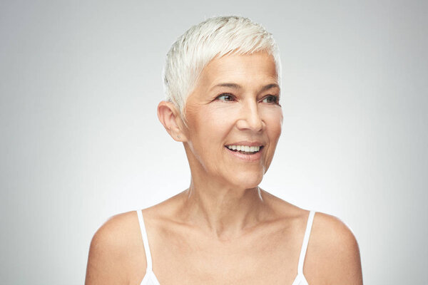Улыбающаяся пожилая женщина с короткими седыми волосами позирует на заднем плане. Фотография красоты
.