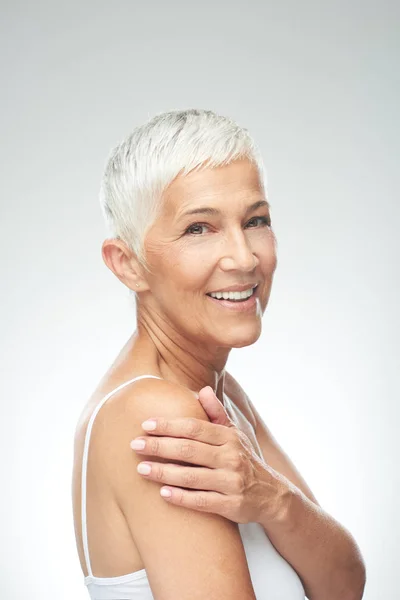 Belle femme âgée souriante aux cheveux gris courts posant devant un fond gris. Photographie beauté . — Photo