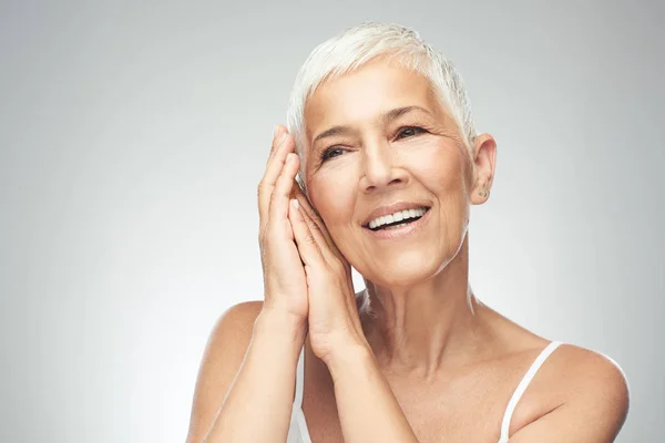 Hermosa mujer mayor sonriente con el pelo gris corto posando delante de fondo gris. Belleza fotografía . —  Fotos de Stock