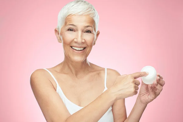 Preciosa sonriente mujer mayor caucásica probando nueva crema anti edad y mirando a la cámara. Belleza fotografía . —  Fotos de Stock