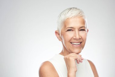 Gri arka plan önünde poz kısa gri saçlı güzel gülümseyen yaşlı kadın. Güzellik fotoğrafçılığı.