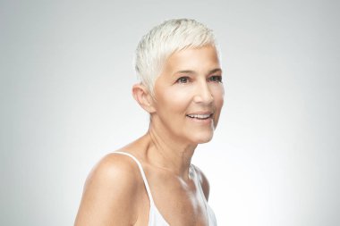 Gri arka plan önünde poz kısa gri saçlı güzel gülümseyen yaşlı kadın. Güzellik fotoğrafçılığı.