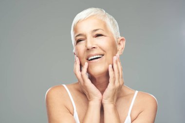 Gri arka plan önünde poz kısa gri saçlı güzel gülümseyen yaşlı kadın. Güzellik fotoğrafçılığı.