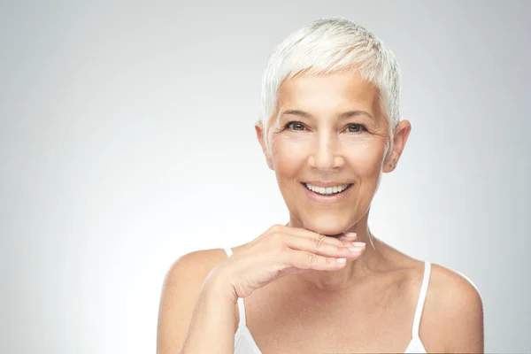 Hermosa mujer mayor sonriente con el pelo gris corto posando delante de fondo gris. Belleza fotografía . — Foto de Stock