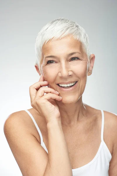 Hermosa mujer mayor sonriente con el pelo gris corto posando delante de fondo gris. Belleza fotografía . — Foto de Stock