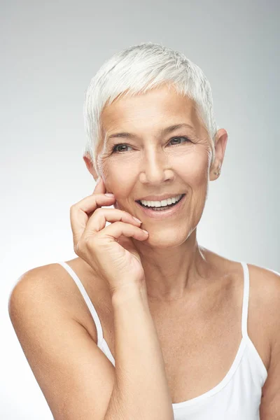 Beautiful smiling senior woman with short gray hair posing in front of gray background. Beauty photography. Stock Picture