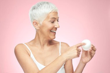 Muhteşem gülümseyen Kafkas yaşlı kadın yeni anti age krem çalışıyor ve kamera bakıyor. Güzellik fotoğrafçılığı.