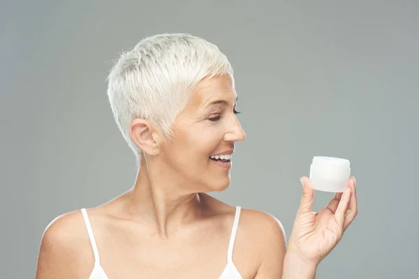 Eine zauberhaft lächelnde kaukasische Seniorin probiert eine neue Anti-Age-Creme aus und blickt in die Kamera. Schönheitsfotografie. — Stockfoto