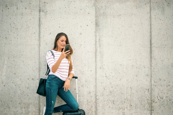 Kobieta za pomocą inteligentnego telefonu jednocześnie opierając się na bagaż na ulicy. — Zdjęcie stockowe