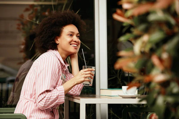Krásná usmívající se smíšená závodní žena, která sedí v kavárně a pije limonádu. — Stock fotografie