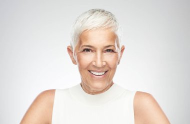 Gri arka plan önünde poz kısa gri saçlı güzel gülümseyen yaşlı kadın. Güzellik fotoğrafçılığı.