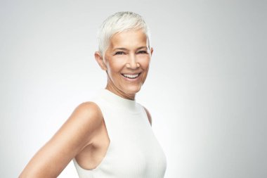 Gri arka plan önünde poz kısa gri saçlı güzel gülümseyen yaşlı kadın. Güzellik fotoğrafçılığı.