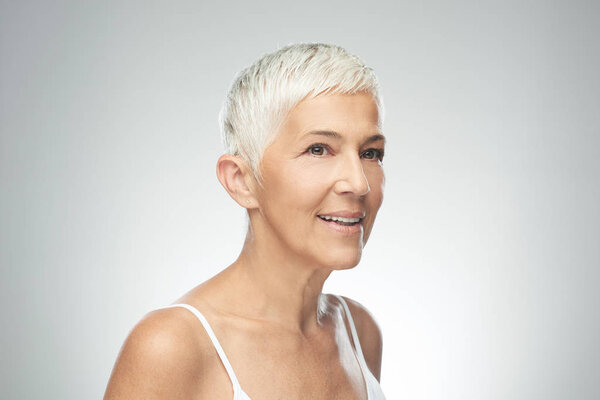 Улыбающаяся пожилая женщина с короткими седыми волосами позирует на заднем плане. Фотография красоты
.