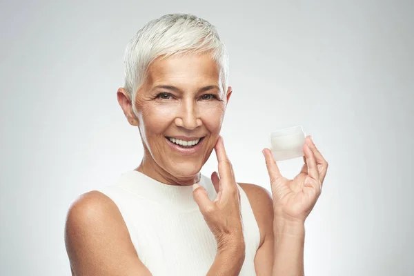 Gorgeous leende kaukasiska Senior Kvinna provar nya anti age Cream. Skönhet fotografi. — Stockfoto
