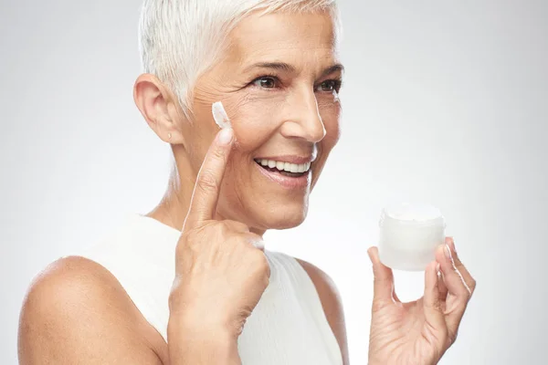 Preciosa sonriente mujer mayor caucásica probando nueva crema anti edad. Belleza fotografía . —  Fotos de Stock