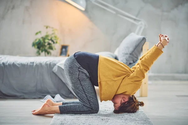 Schöne kaukasische Brünette macht Kopfstand Yoga-Pose im Schlafzimmer auf Teppich. — Stockfoto