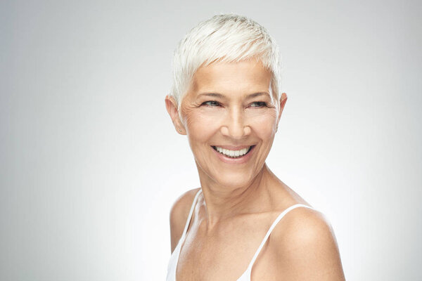 Улыбающаяся пожилая женщина с короткими седыми волосами позирует на заднем плане. Фотография красоты
.