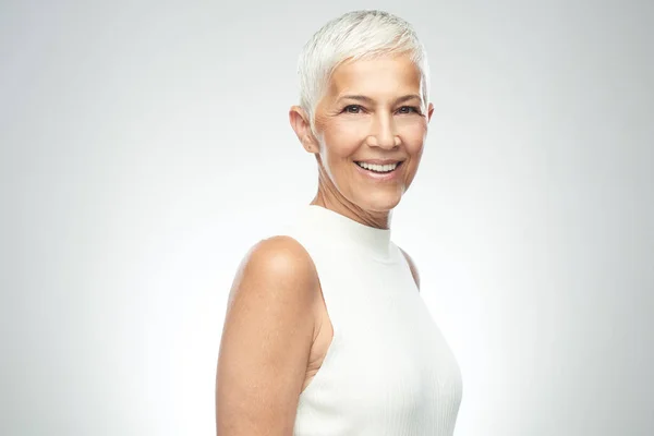 Hermosa mujer mayor sonriente con el pelo gris corto posando delante de fondo gris. Belleza fotografía . — Foto de Stock