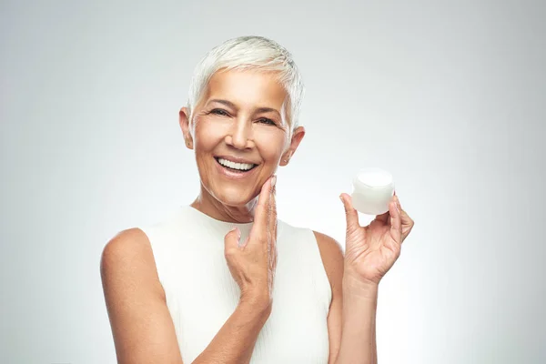 Gorgeous leende kaukasiska Senior Kvinna provar nya anti age Cream. Skönhet fotografi. — Stockfoto