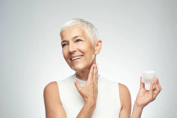 Gorgeous smiling Caucasian senior woman trying out new anti age cream. Beauty photography.