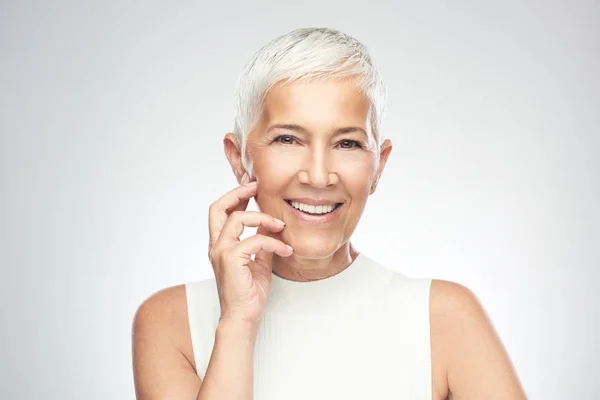 Hermosa mujer mayor sonriente con el pelo gris corto posando delante de fondo gris. Belleza fotografía . — Foto de Stock