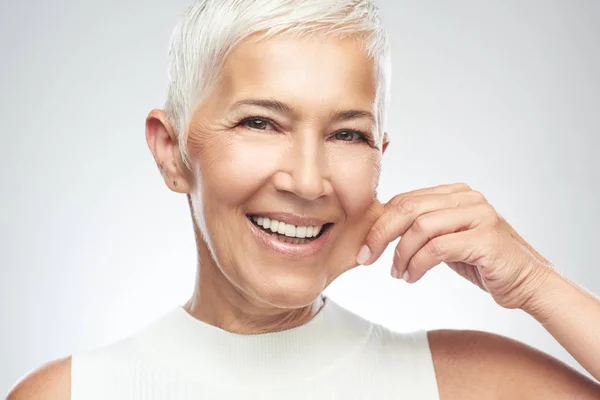 Preciosa mujer mayor caucásica sonriente con el pelo gris corto pellizcando su mejilla. Belleza fotografía . —  Fotos de Stock