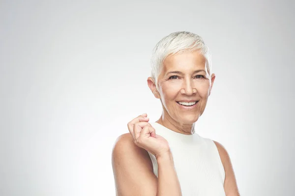 Bella donna anziana sorridente con i capelli corti grigi in posa di fronte a sfondo grigio. Foto di bellezza . — Foto Stock