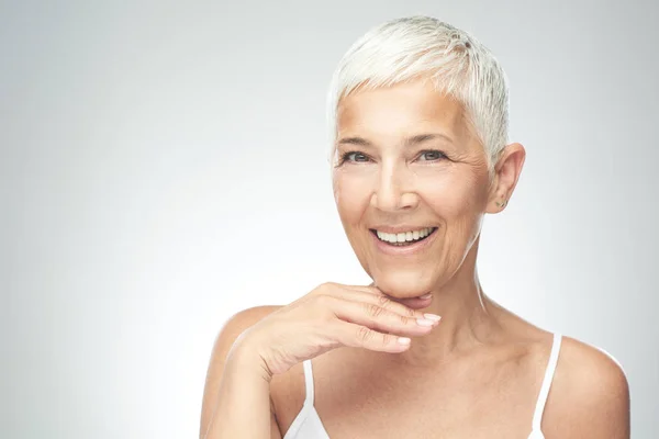 Beautiful smiling senior woman with short gray hair posing in front of gray background. Beauty photography. Stock Image