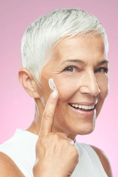 Великолепная улыбающаяся белая пожилая женщина пробует новый антивозрастной крем. Фотография красоты . — стоковое фото