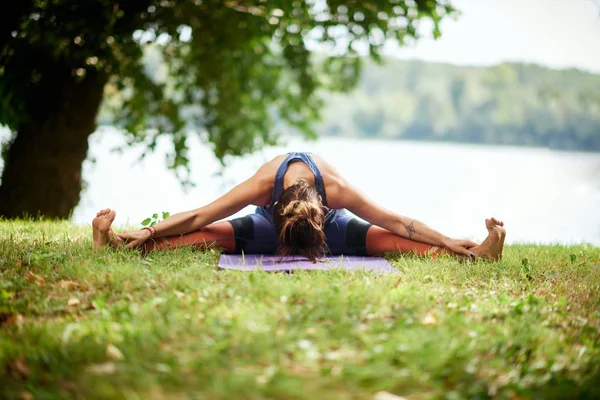 Dedicato donna caucasica seduta sul tappeto in natura vicino all'acqua e facendo seduto a gambe larghe piega avanti yoga posa . — Foto Stock