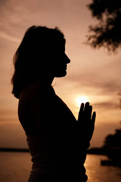 Silueta de mujer de pie en posición de oración al atardecer. Concepto de ejercicio de yoga . —  Fotos de Stock