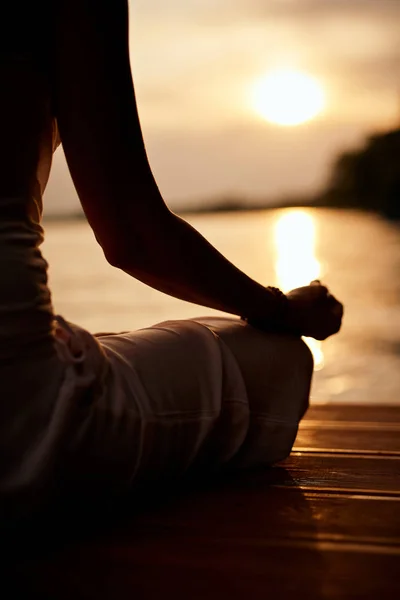 Rear view of Caucasian woman sitting in lotus position and meditating on dock at sunset. — Stock Photo, Image