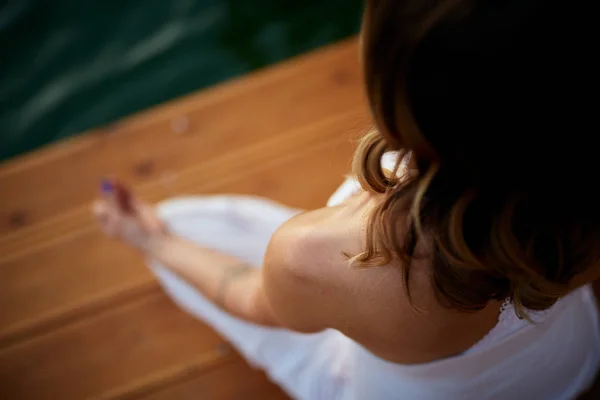 Vista superior de la mujer caucásica sentada en el muelle en posición de loto y meditando. Hora de verano . — Foto de Stock